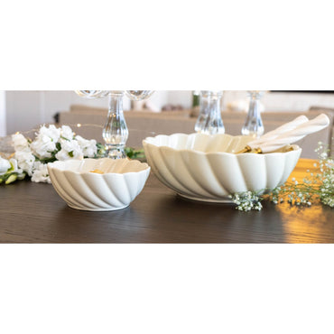 Two white decorative bowls on a table with flowers and candles in the background.