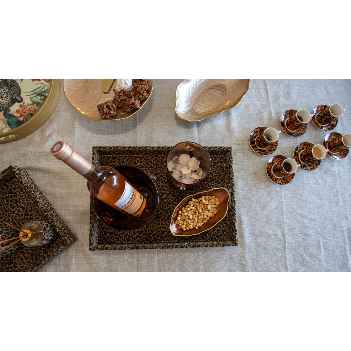 Wine bottle on a decorative coaster with snacks and glasses on a tablecloth.