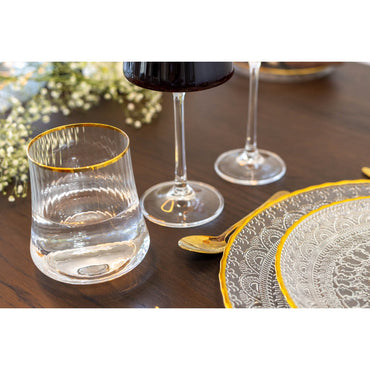 Clear glass with gold rim on a wooden table with wine glasses and decorative plates.