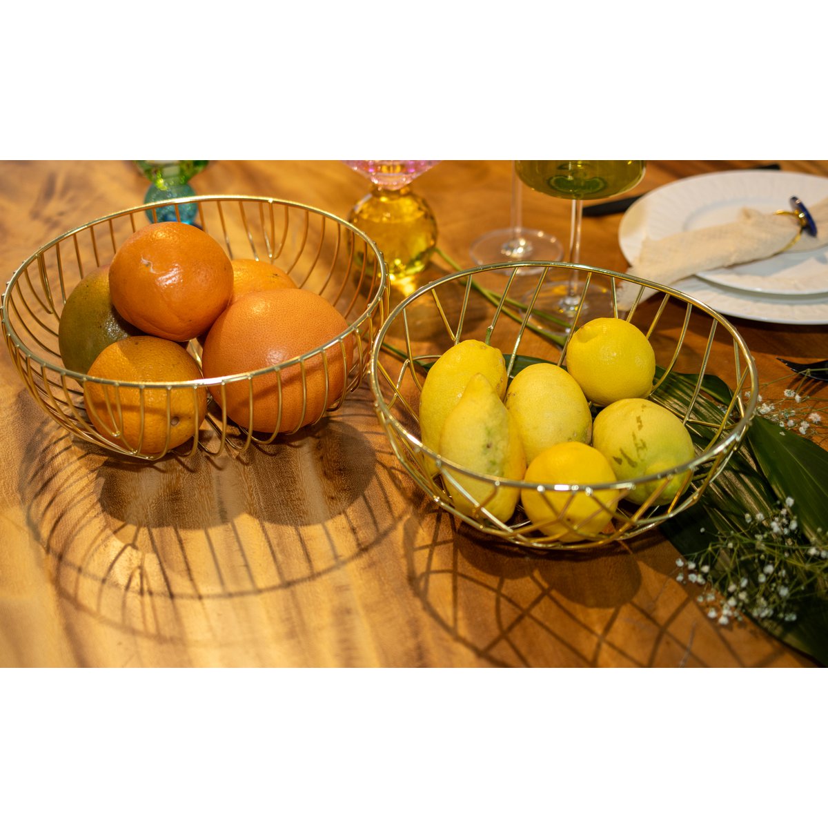 Two wire baskets filled with oranges and lemons on a wooden table.