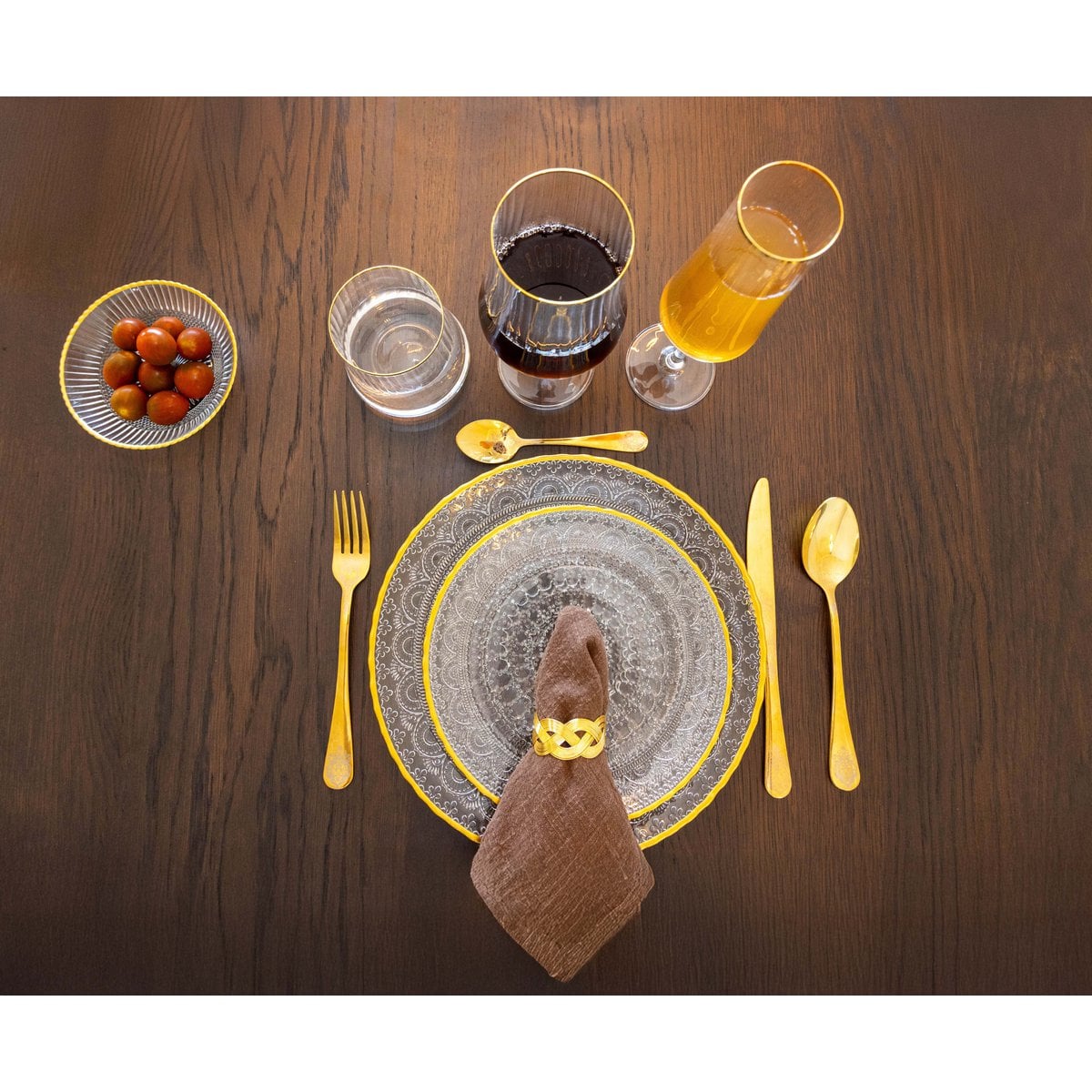 Dinner table setting with glassware, cutlery, and a plate on a wooden surface.