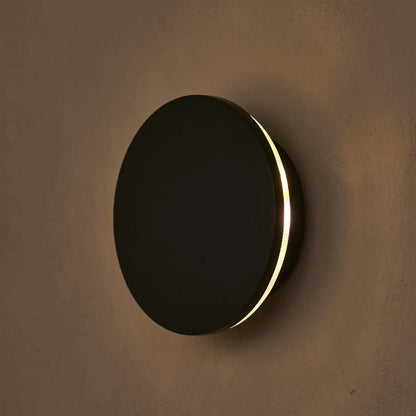 Round wall light fixture with black finish and gold rim on a brown wall.